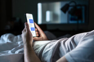 Eine Person liegt im Bett und liest Nachrichten auf ihrem Smartphone, als Symbol für Heimlichkeit, Affären und Vertrauensbruch in einer Paarbeziehung.